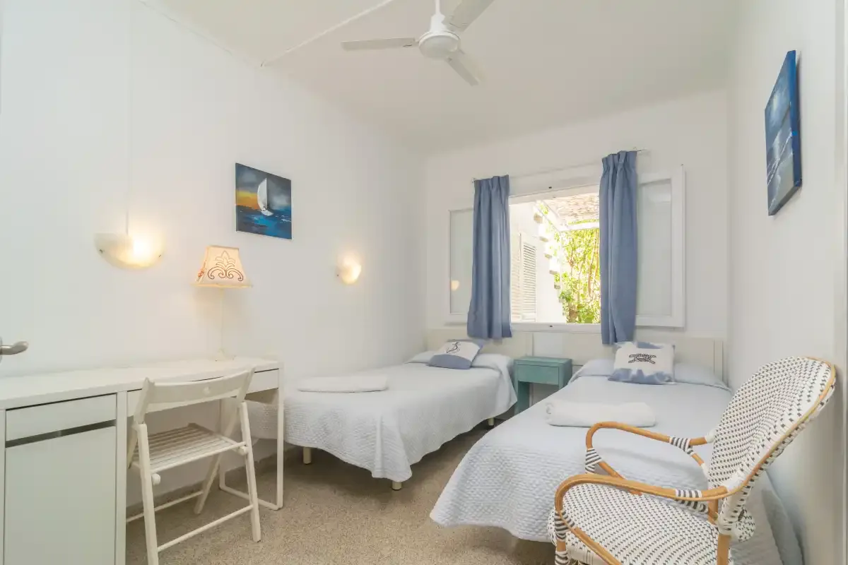 Un dormitorio luminoso con dos camas, un escritorio y una ventana con cortinas azules.