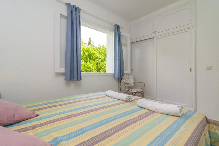 Un dormitorio con una colcha a rayas, una ventana abierta y cortinas azules.