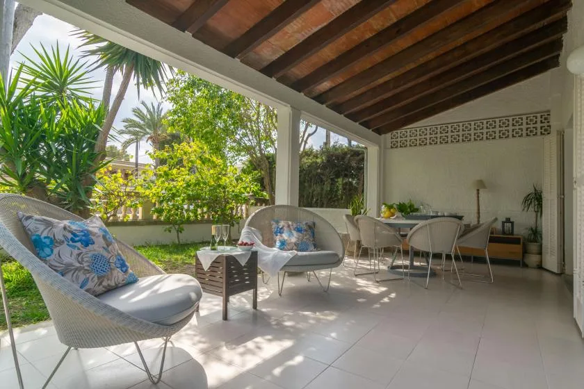 Un patio cubierto con asientos exteriores y una mesa de comedor da a un jardín frondoso.