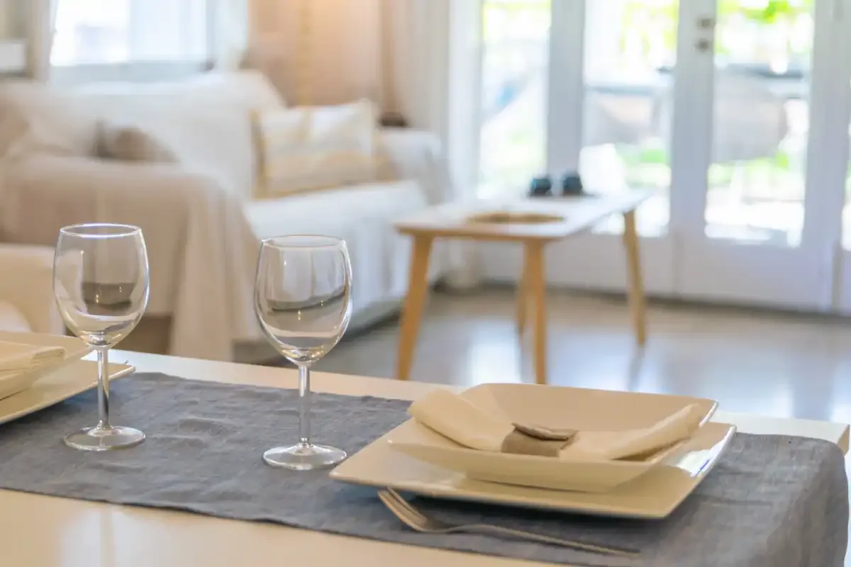 Una sala luminosa con una mesa de comedor preparada con platos y copas.