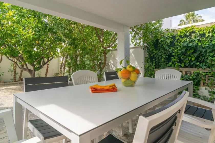 Comedor exterior cubierto con una mesa blanca y vegetación frondosa.