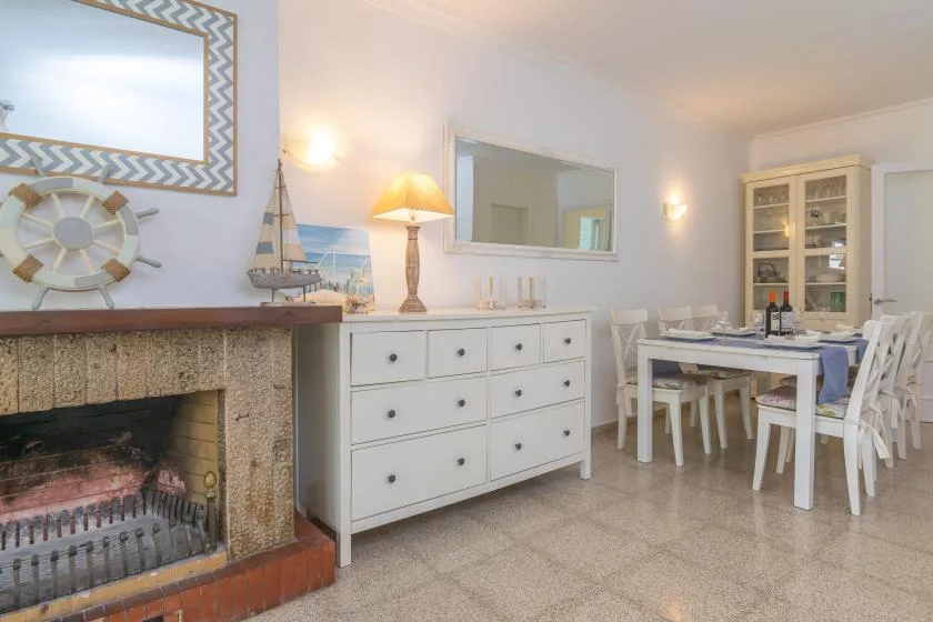 Comedor con mesa y sillas junto a una chimenea y una cómoda blanca.