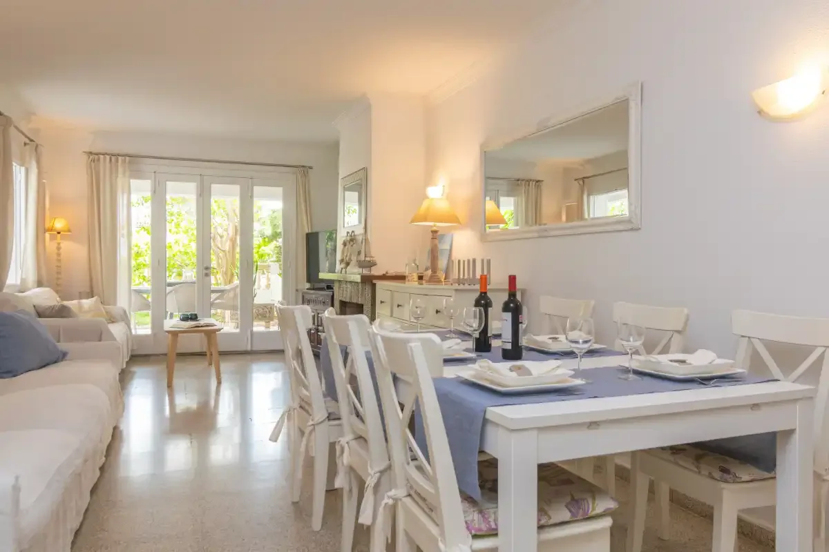 Un luminoso comedor y sala de estar, con la mesa puesta y asientos junto a puertas acristaladas.