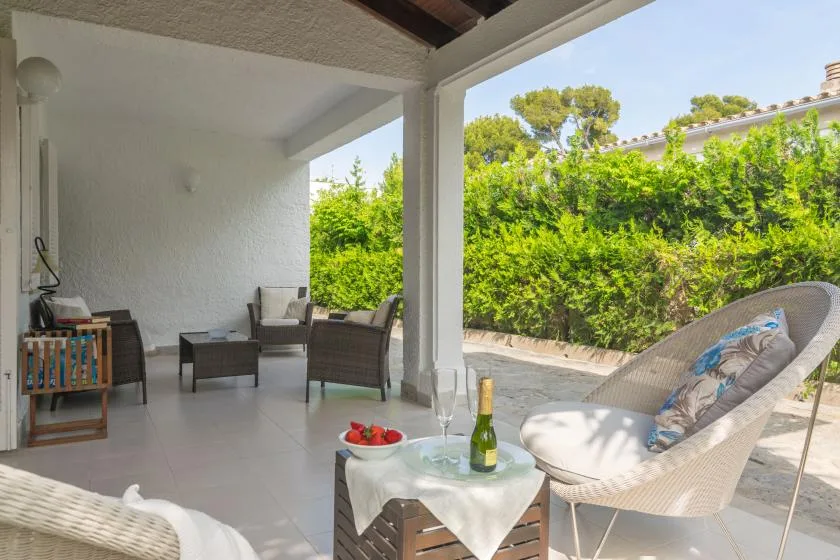 Un patio cubierto con asientos de exterior y una mesa pequeña da a un seto verde.