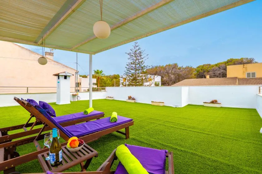 Una terraza en la azotea tiene asientos morados sobre césped verde bajo un toldo.