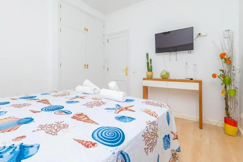 Un dormitorio luminoso con una cama cubierta de estampados marinos azules y coral.