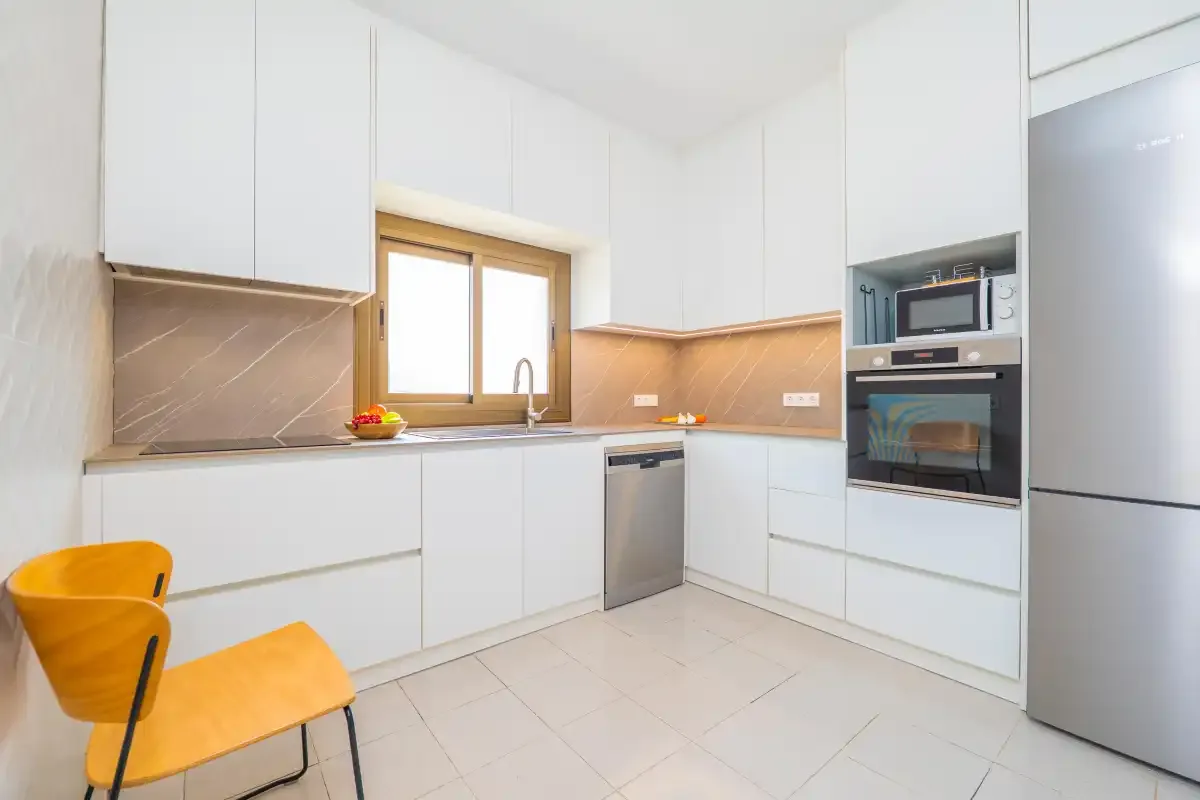 Una cocina luminosa con armarios blancos, fregadero y electrodomésticos integrados.