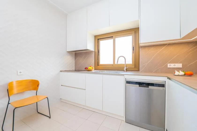 Una cocina luminosa con armarios blancos, una encimera y una ventana sobre el fregadero.