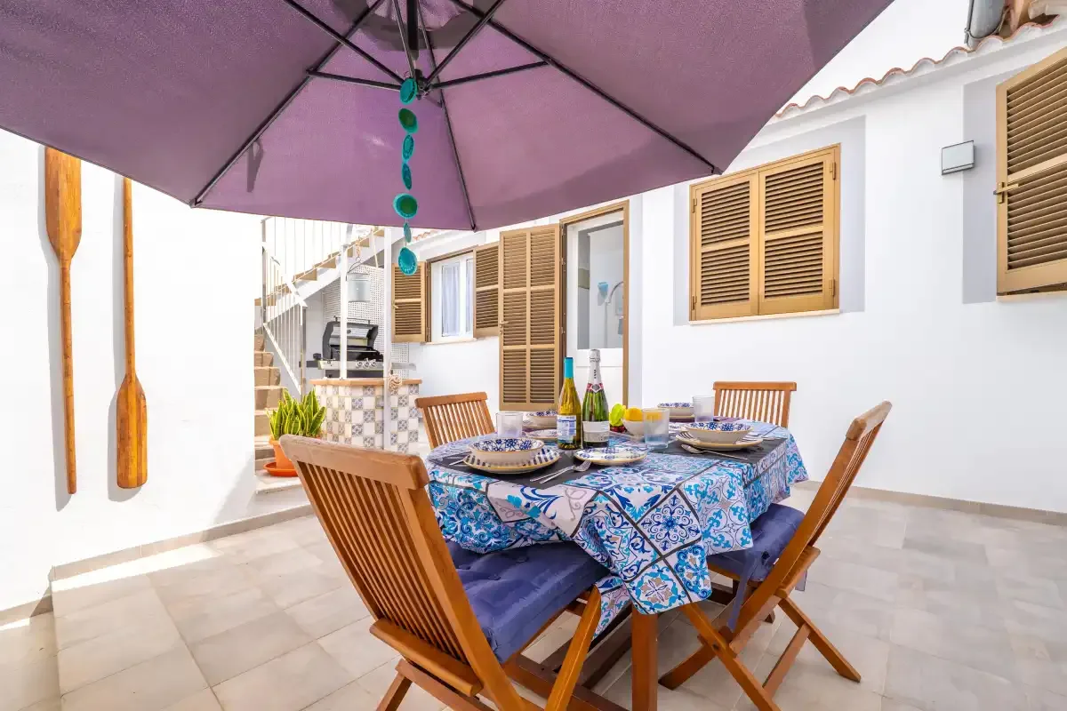 Una zona de comedor al aire libre con un mantel estampado bajo una sombrilla grande.