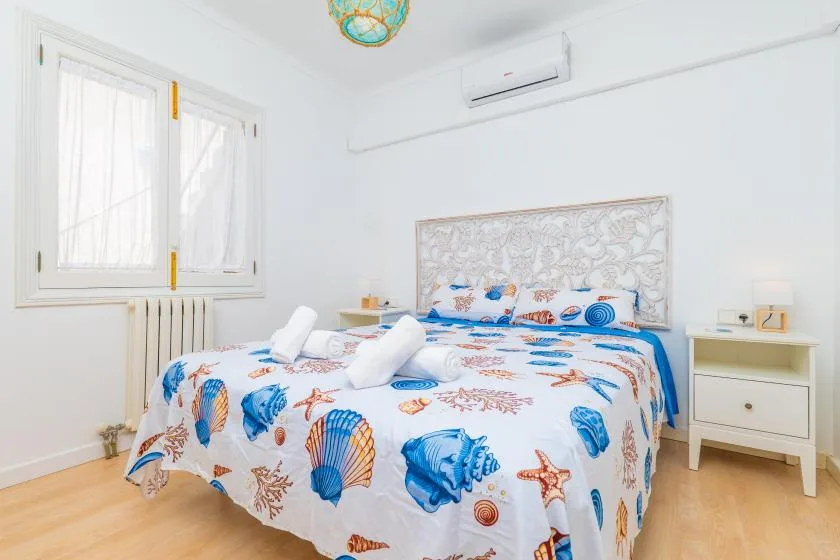 Un dormitorio luminoso con una cama cubierta de motivos de conchas azules y naranjas.