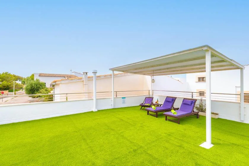 Una terraza en la azotea con césped sintético, asientos y una pérgola cubierta.