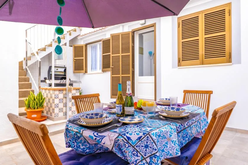 Una zona de comedor al aire libre tiene una mesa puesta bajo una sombrilla morada.
