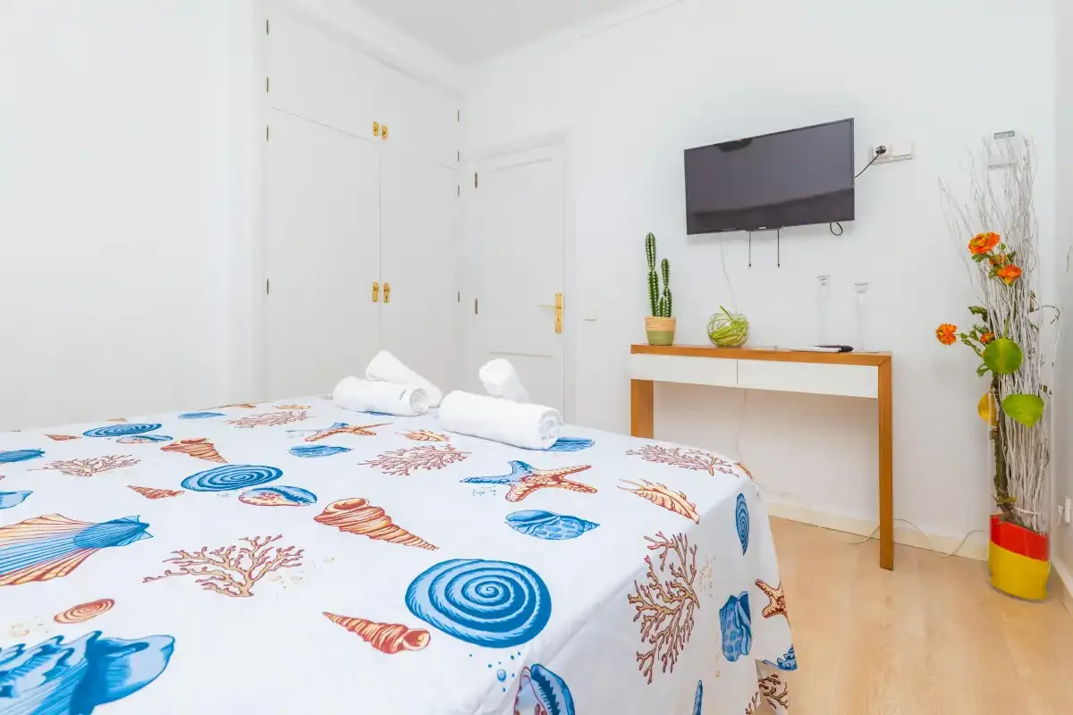 Un dormitorio con una cama cubierta de motivos de conchas azules y naranjas y un televisor en la pared.