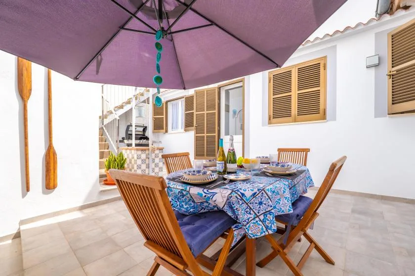 Un comedor exterior con suelo de baldosas y una mesa bajo una gran sombrilla.