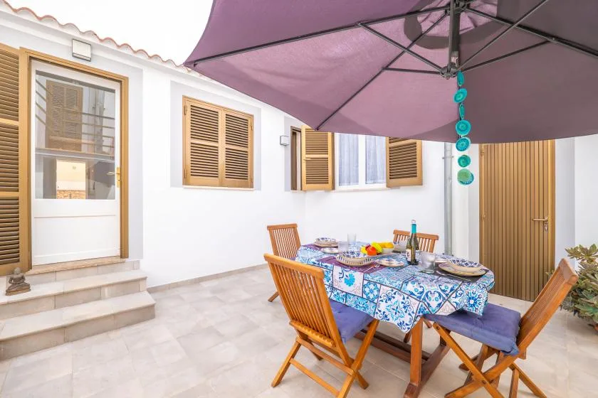 Comedor exterior con suelo de baldosas, mesa y asientos de madera bajo una gran sombrilla.