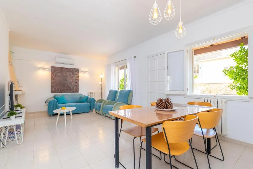 Una luminosa sala de estar y comedor con asientos turquesa y una mesa de madera.