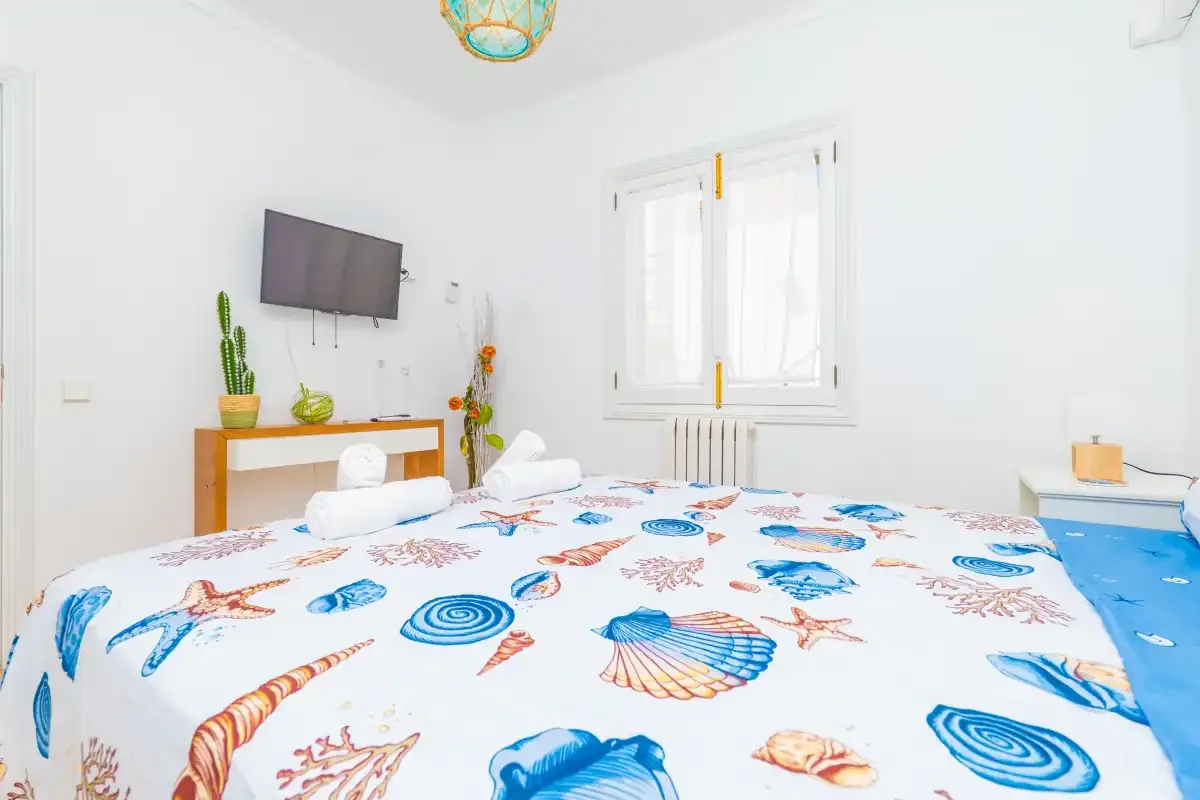 Un dormitorio luminoso con una cama cubierta de estampados coloridos de conchas y estrellas de mar.