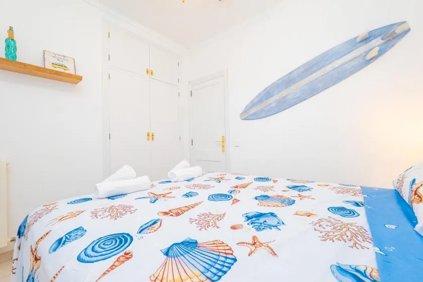 Un dormitorio con una cama cubierta de estampados marinos azules y naranjas.