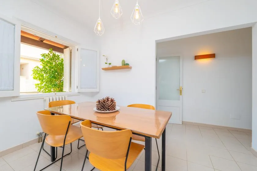 Un comedor luminoso tiene una mesa de madera y asientos junto a una ventana abierta.