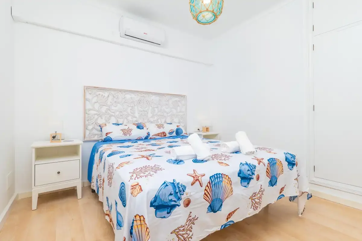 Un dormitorio luminoso con una cama doble cubierta de motivos marinos azules.