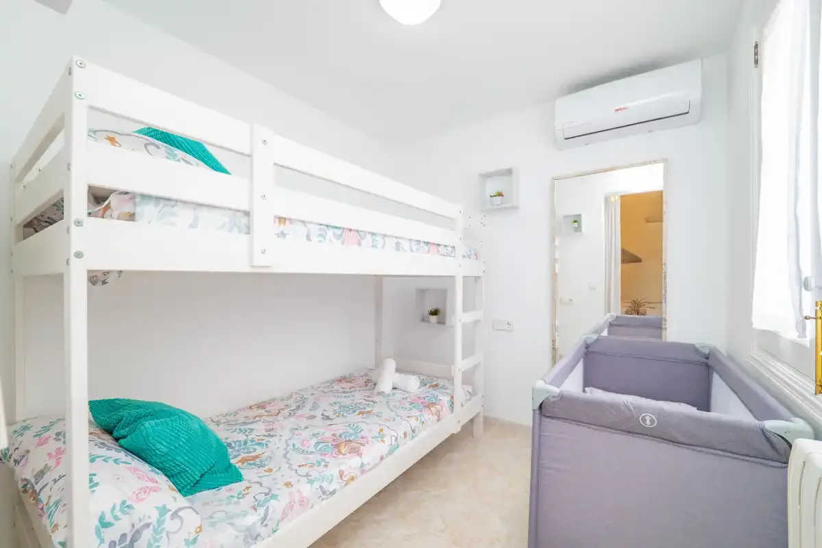 Un dormitorio luminoso con literas y una cuna gris.