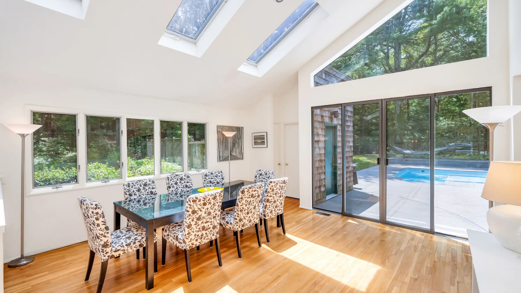 Un comedor luminoso con una mesa y sillas junto a grandes ventanas que dan a una piscina.