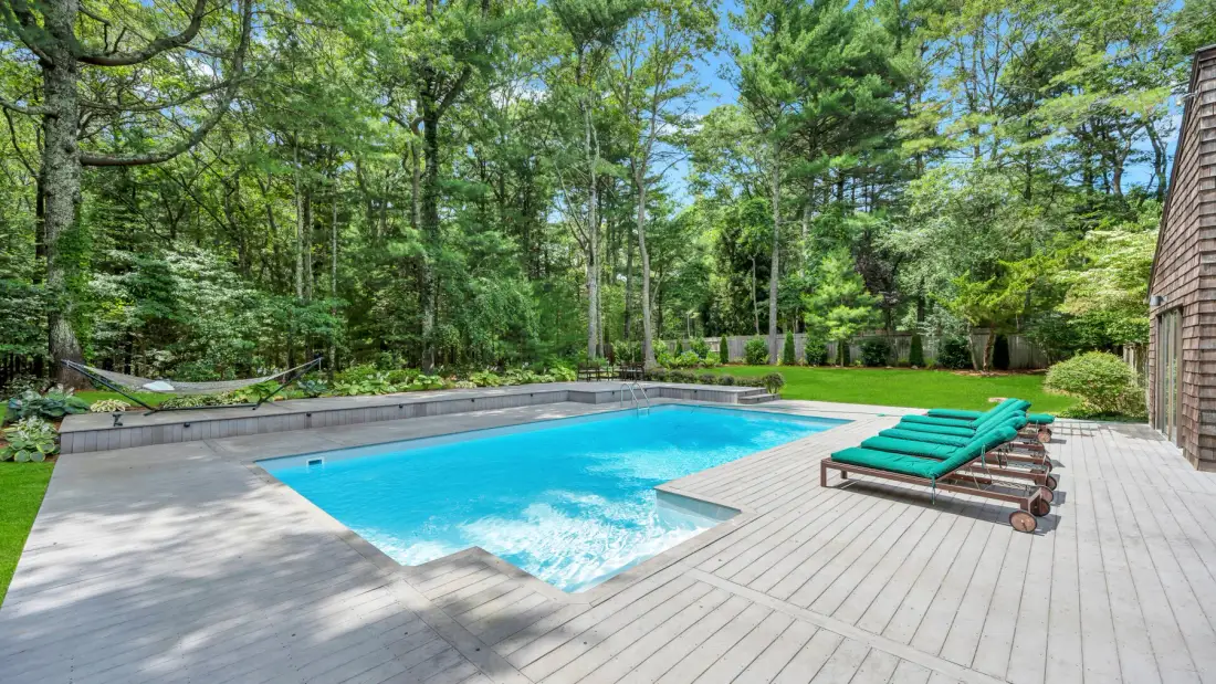 Una piscina al aire libre está junto a una terraza de madera y árboles.