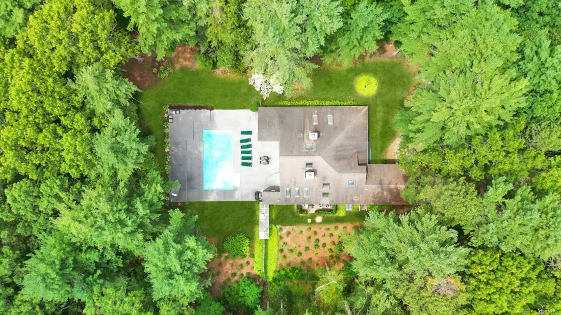 Una vista aérea muestra una piscina y un patio pavimentado rodeados de árboles.