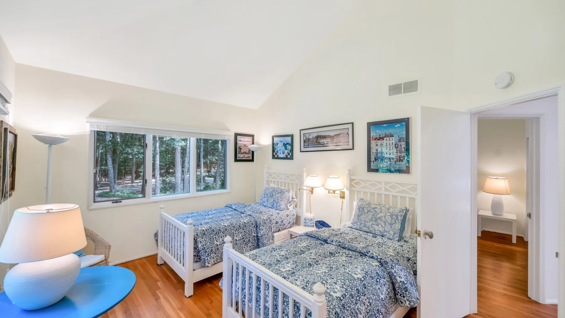 Un dormitorio luminoso con dos camas, una ventana y cuadros enmarcados.