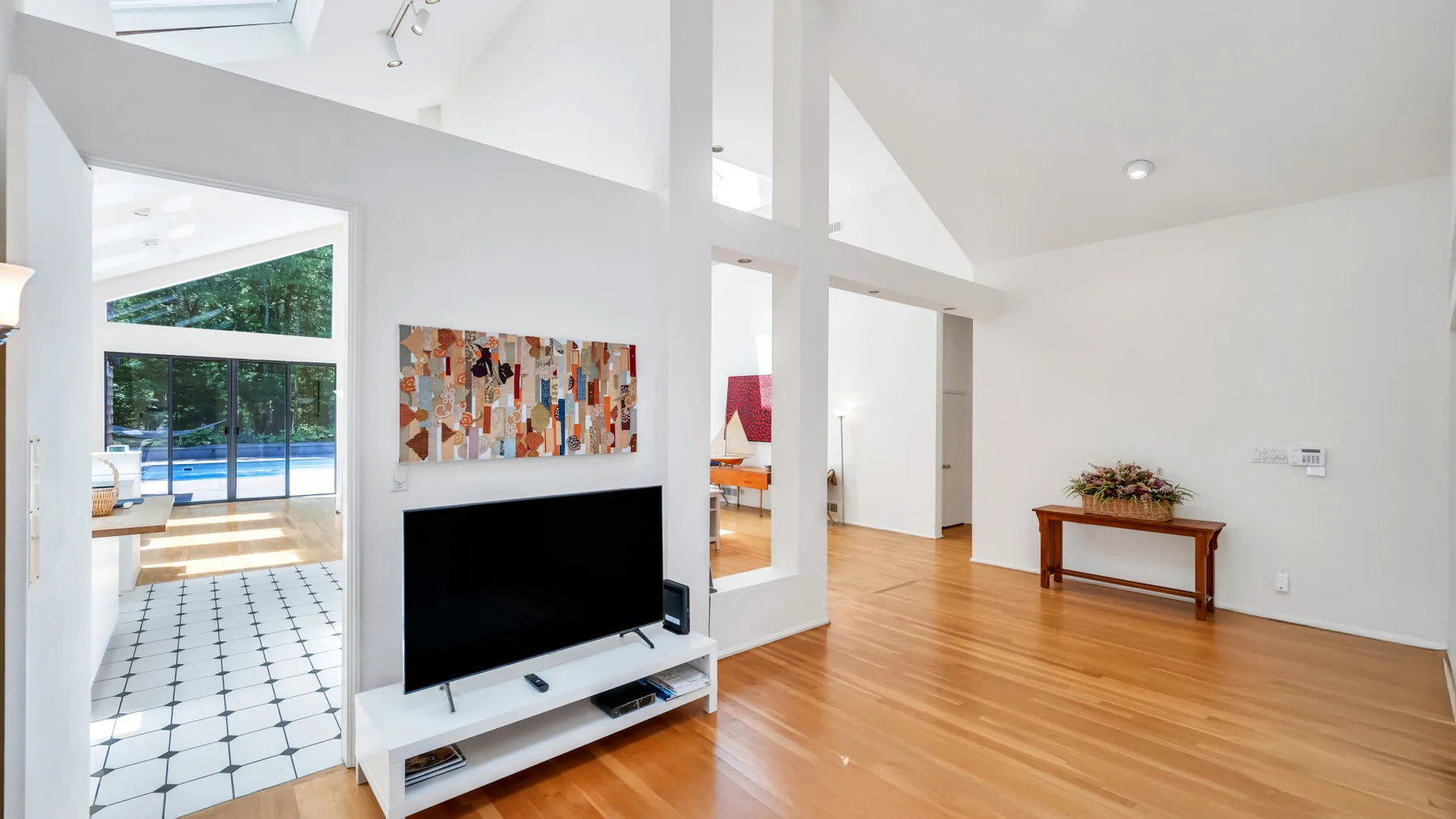 Una luminosa sala de estar tiene un televisor, suelo de madera y vistas abiertas a espacios contiguos.