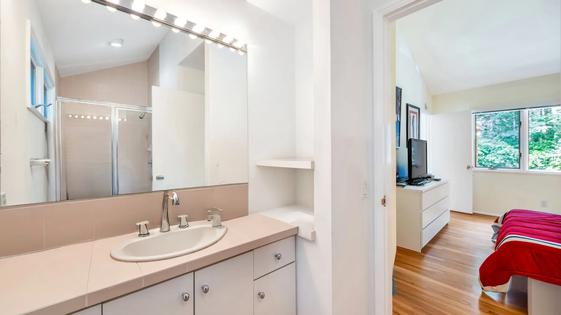 Un lavabo de baño da a un dormitorio con una cama y una ventana.