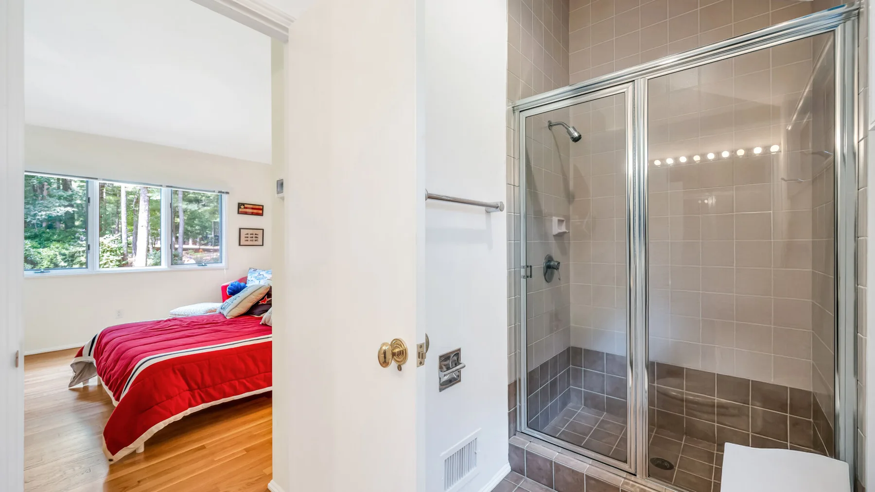 Un dormitorio con una cama roja junto a una ducha con mampara de vidrio.