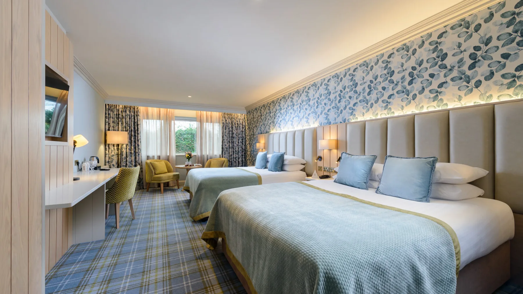 Guest room with two double beds, a desk and armchairs by the window.