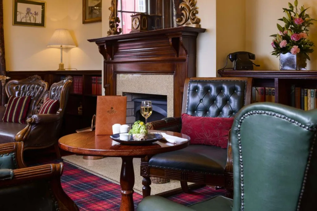 Hotel lounge with green leather chairs, fireplace and bookshelves.