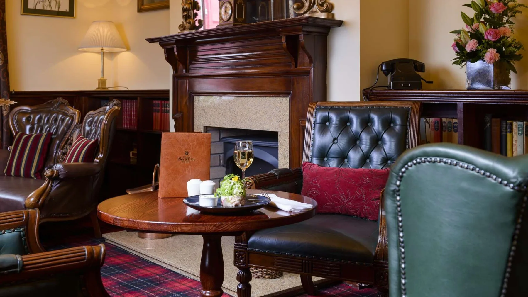 Hotel lounge with green leather chairs, fireplace and bookshelves.