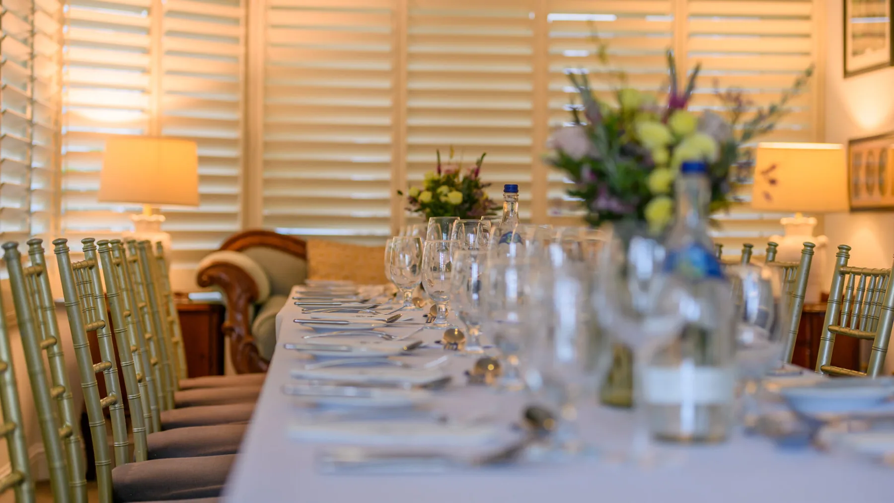 Dining room with a long set table and gold chairs.