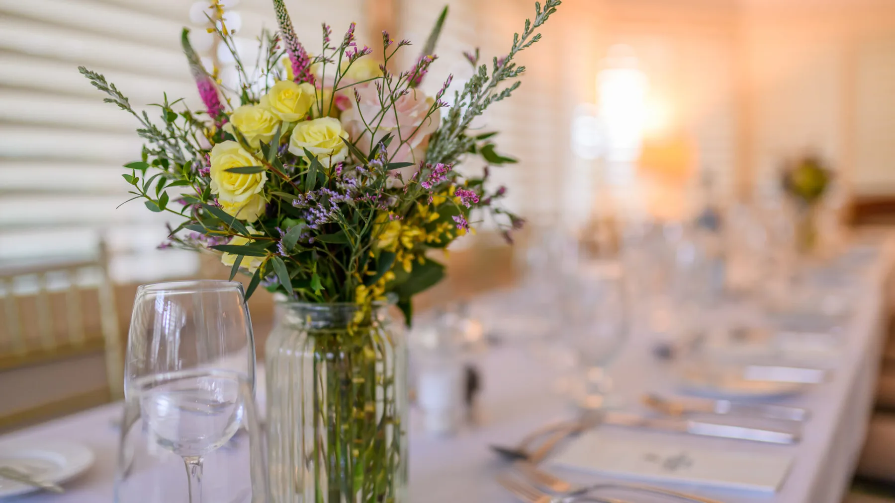 Set dining table with flowers, glassware and place settings.