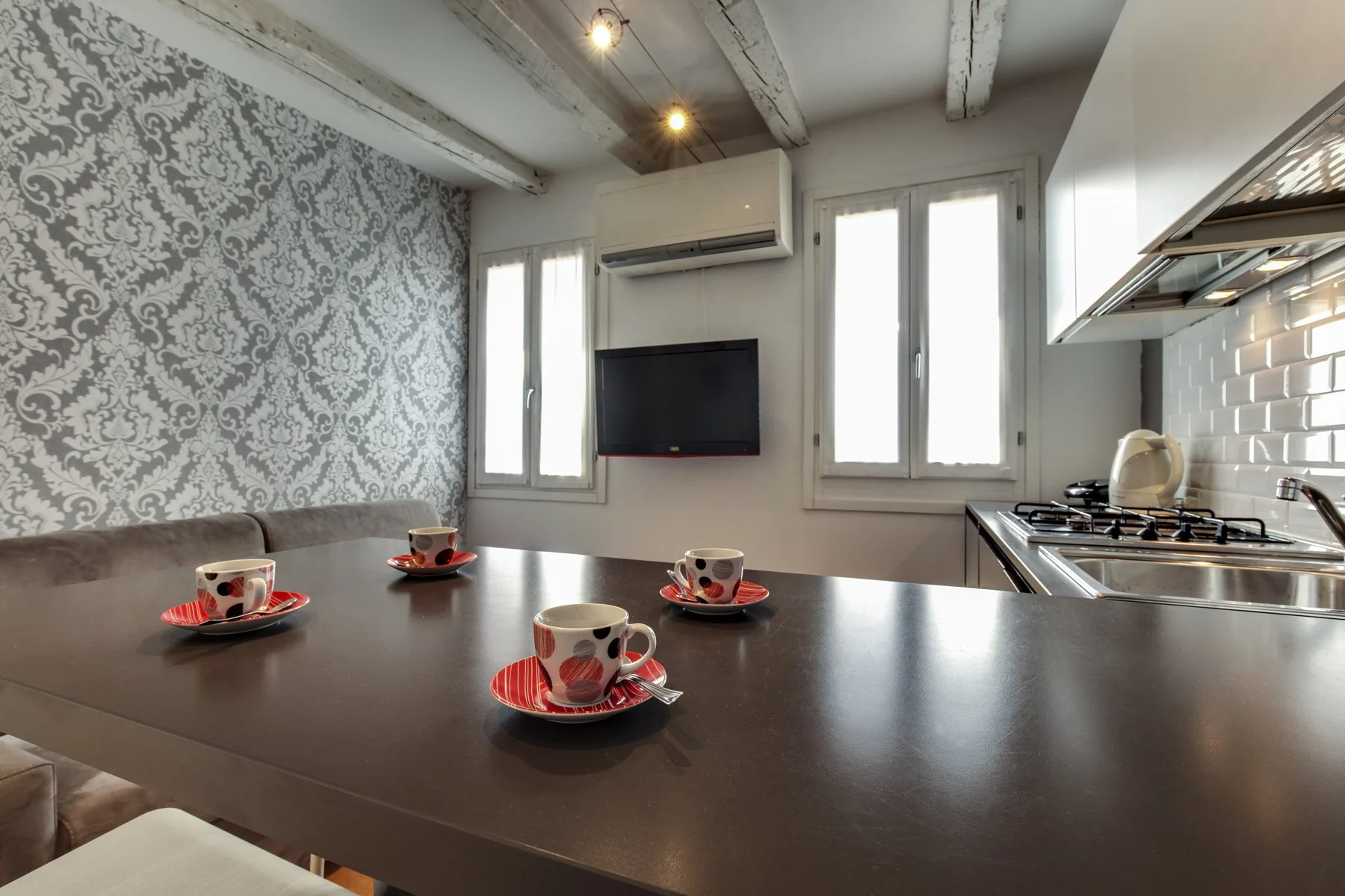 Una cocina y comedor con una mesa oscura preparada con tazas.