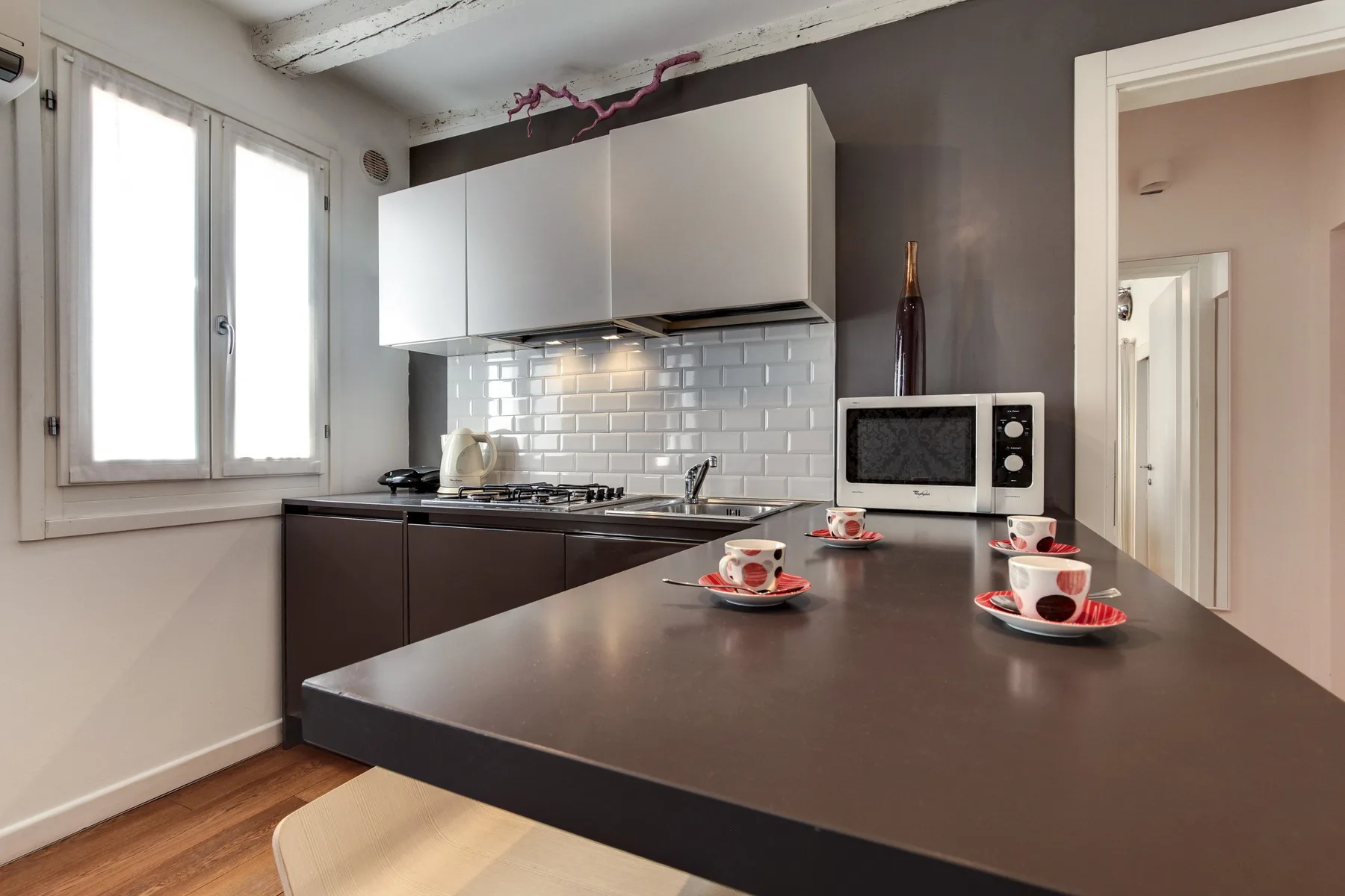 Una cocina con encimeras oscuras, armarios blancos y un salpicadero de azulejos.