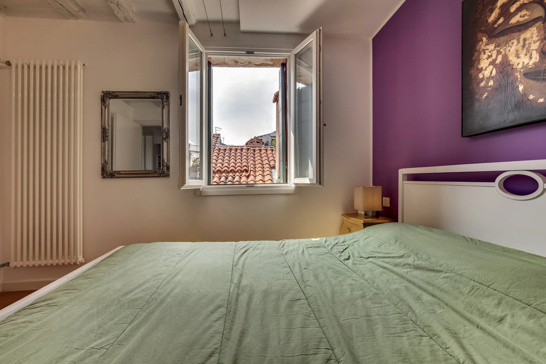 Un dormitorio con una cama bajo una ventana abierta y una pared de acento morada.