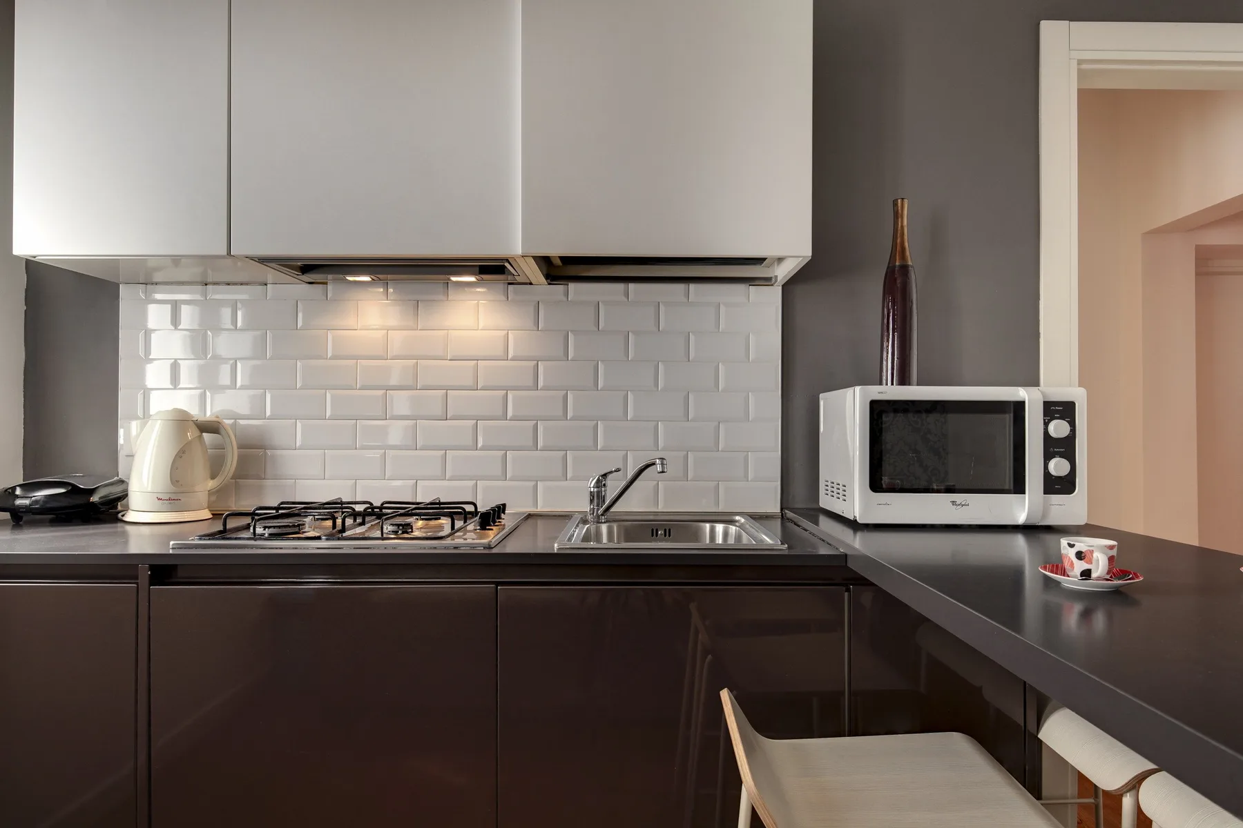 Una cocina moderna con gabinetes oscuros, un salpicadero de azulejos y un microondas sobre la encimera.