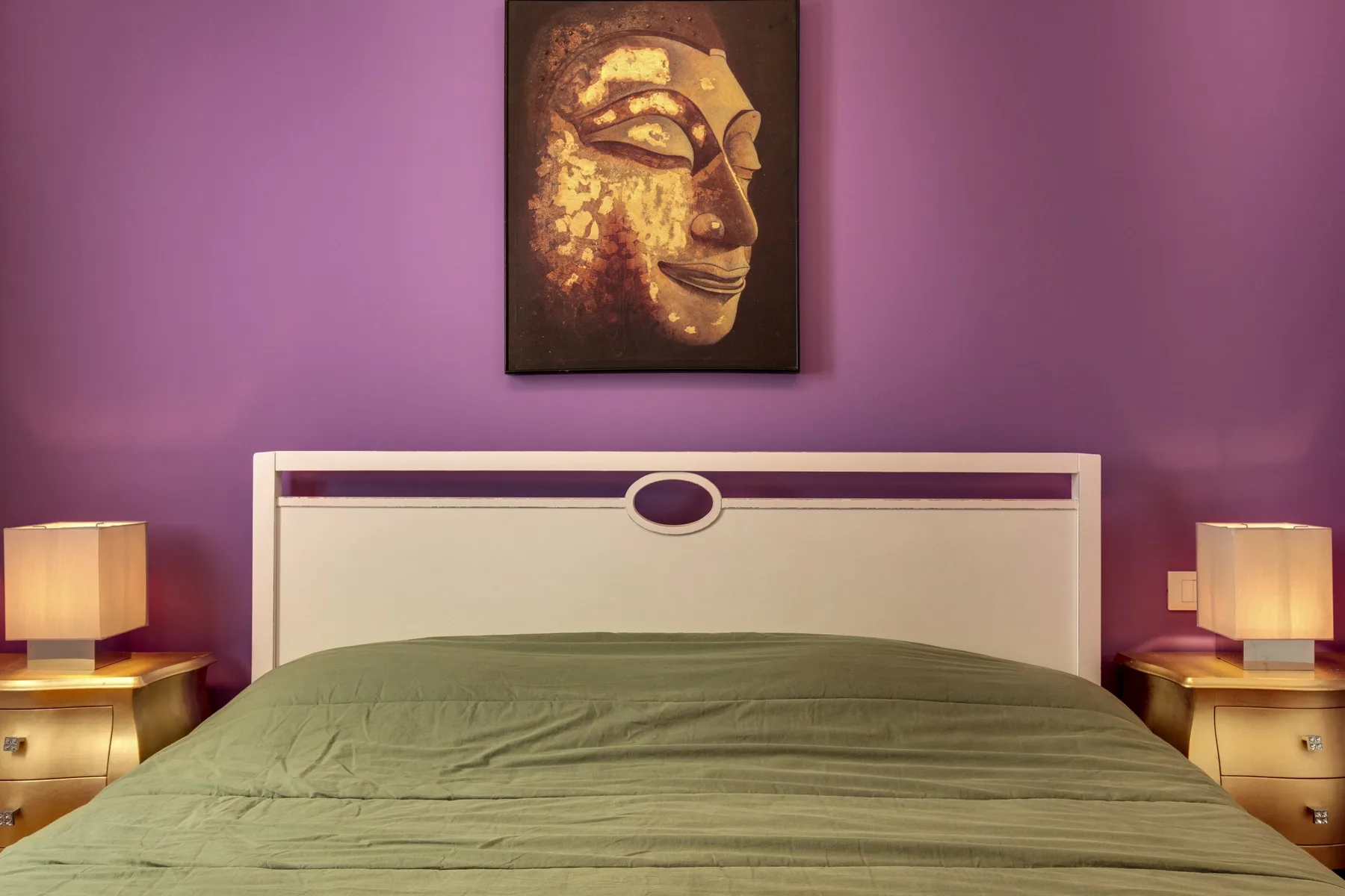 Un dormitorio con una cama junto a una pared morada y un cuadro enmarcado encima.