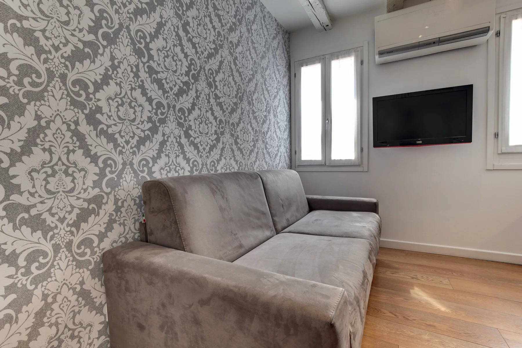 Una sala de estar con un sofá gris y un televisor montado en la pared.