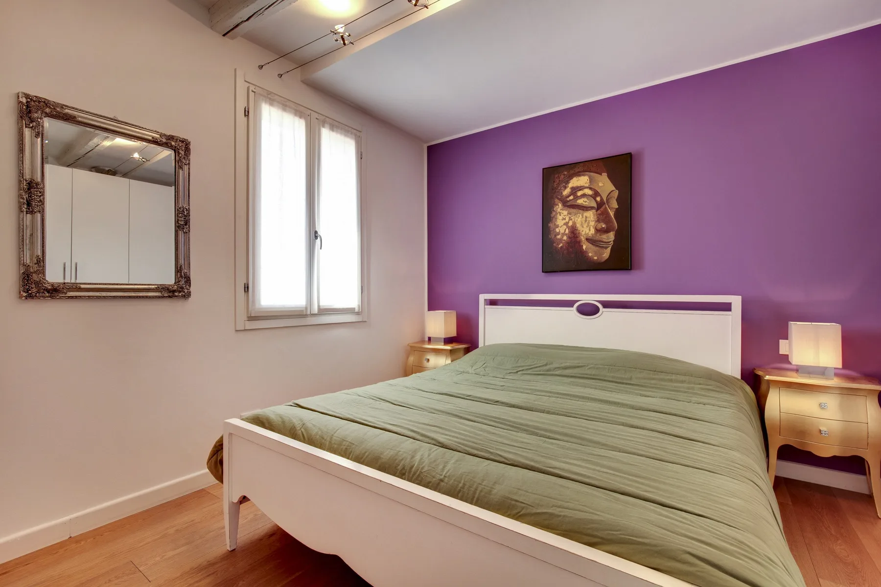 Un dormitorio con una cama blanca, ropa de cama verde y una pared morada.
