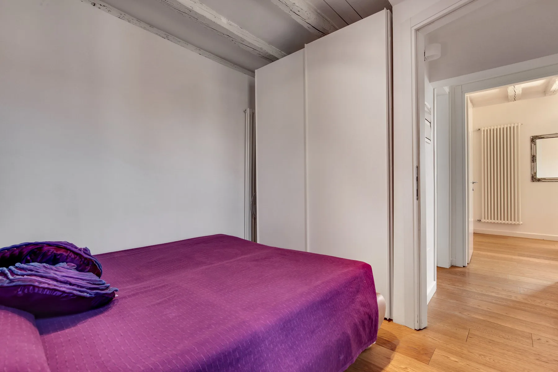 Un dormitorio con una cama cubierta de color morado junto a una puerta abierta.