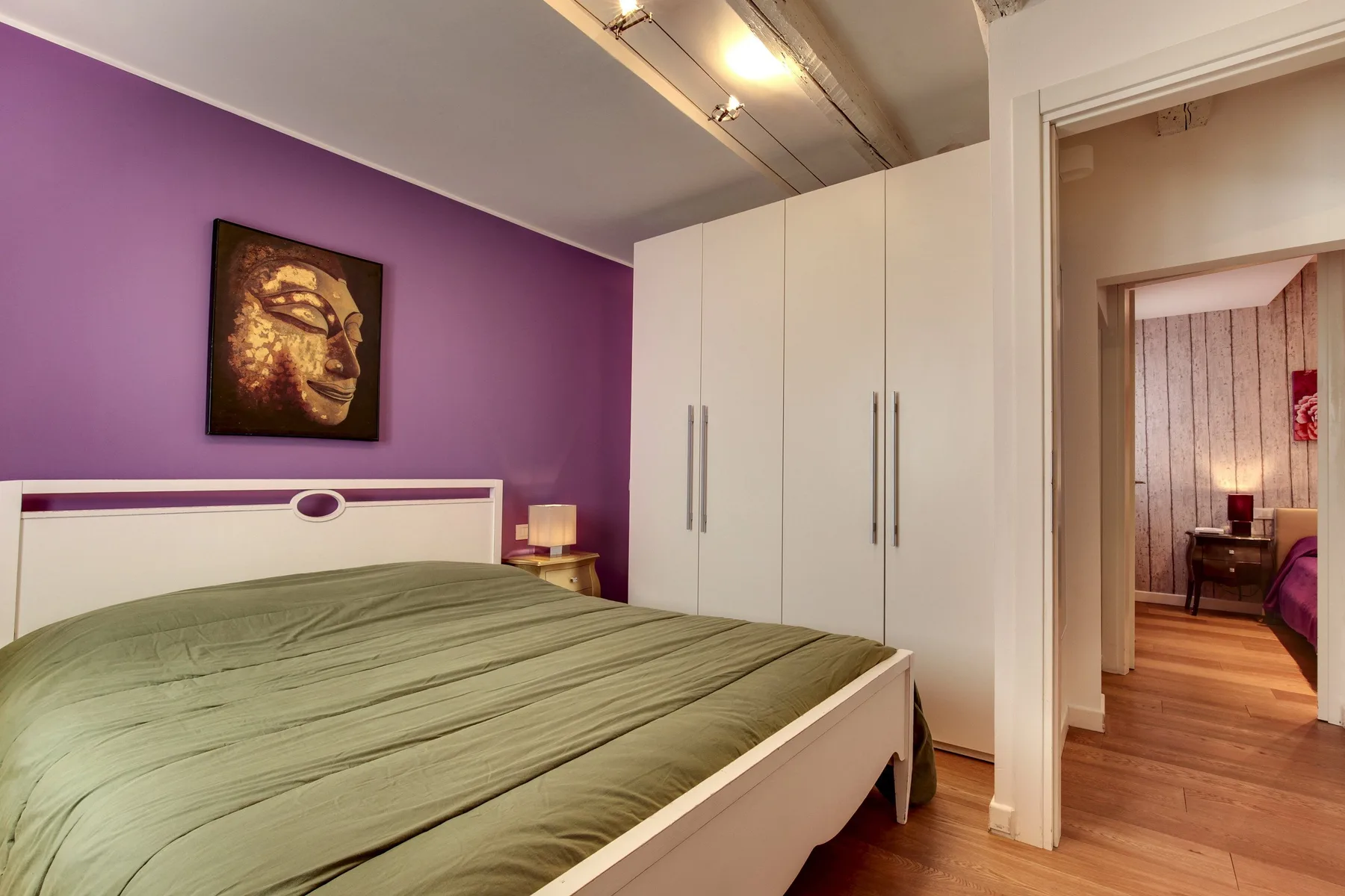 Un dormitorio con una cama, armarios blancos y una pared de acento morada.