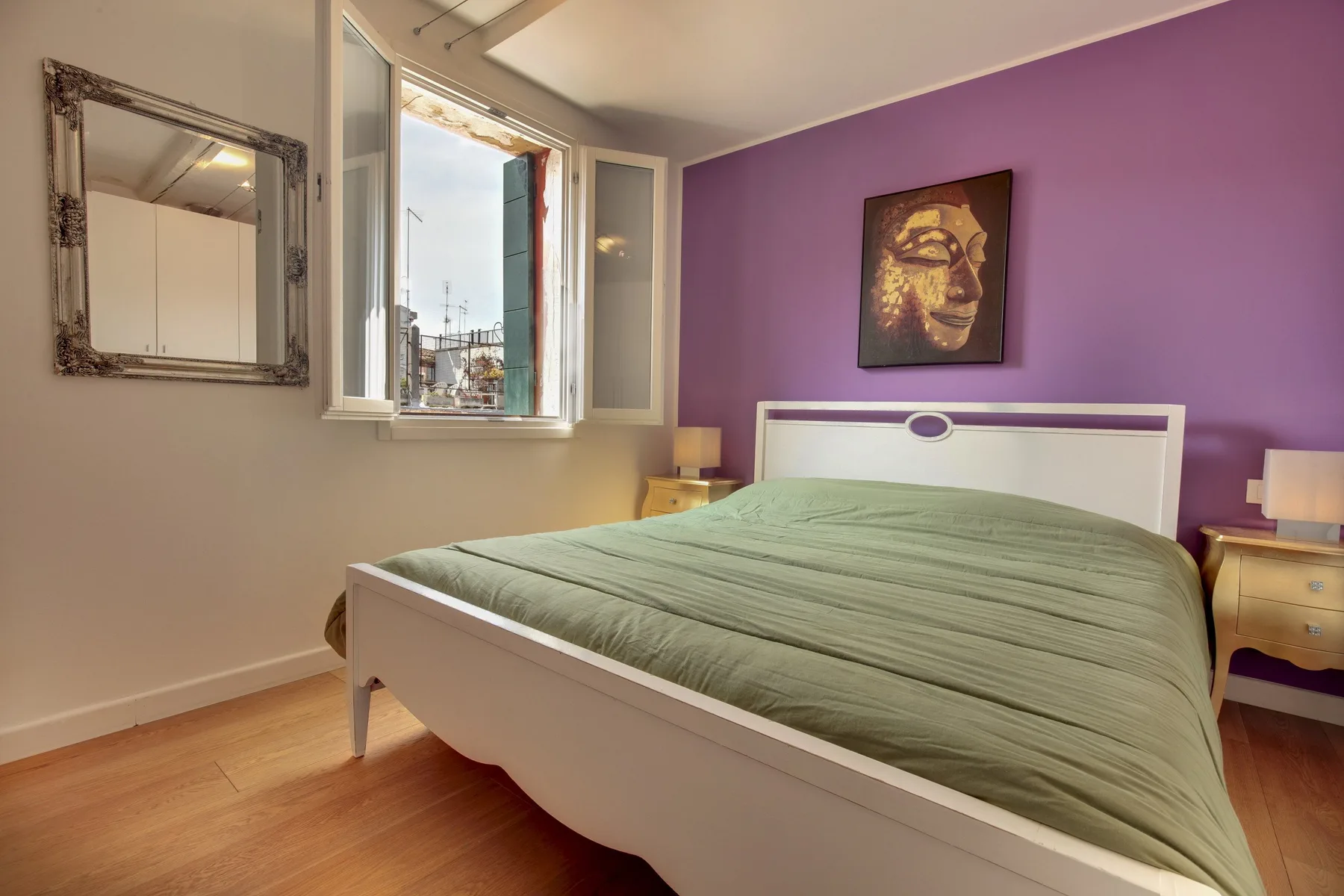 Un dormitorio con una cama blanca, ropa de cama verde y una pared morada.