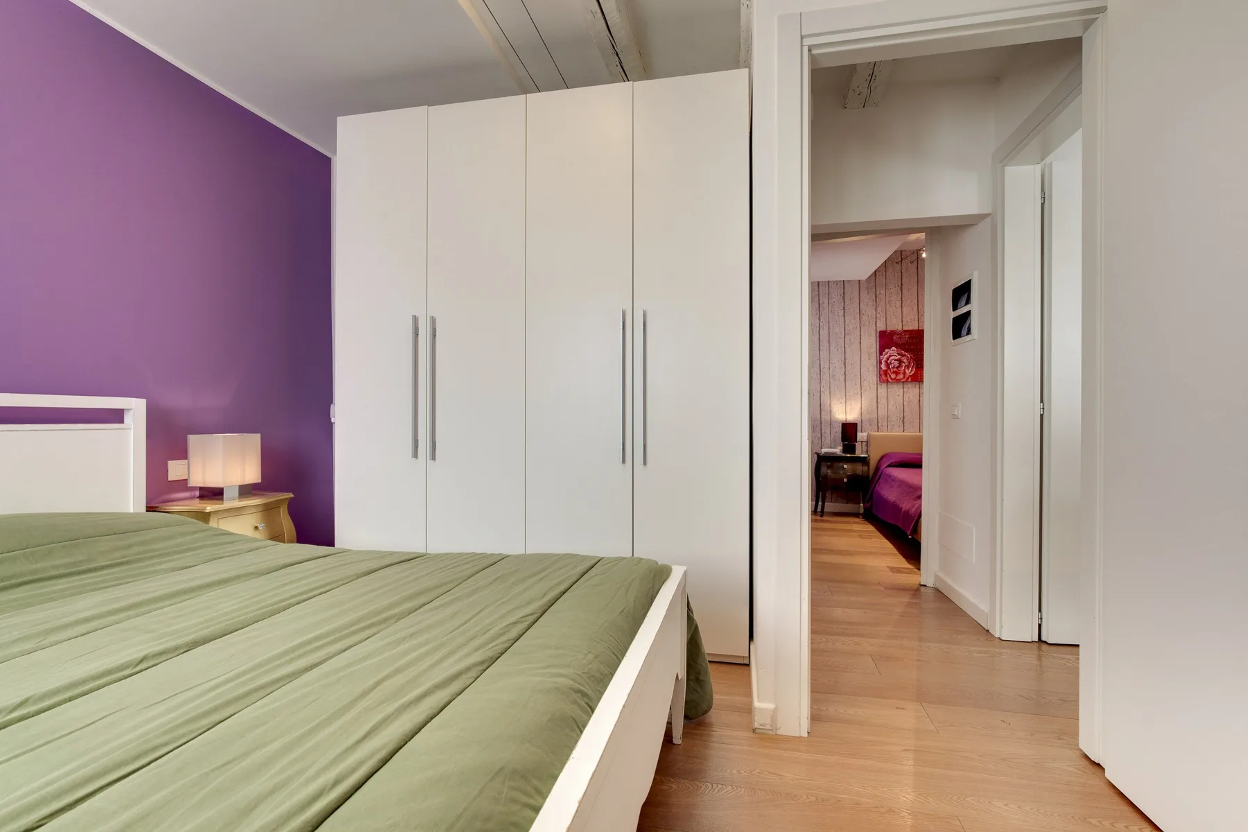 Dormitorio con una cama cubierta de verde, un armario blanco y una puerta hacia otra habitación.