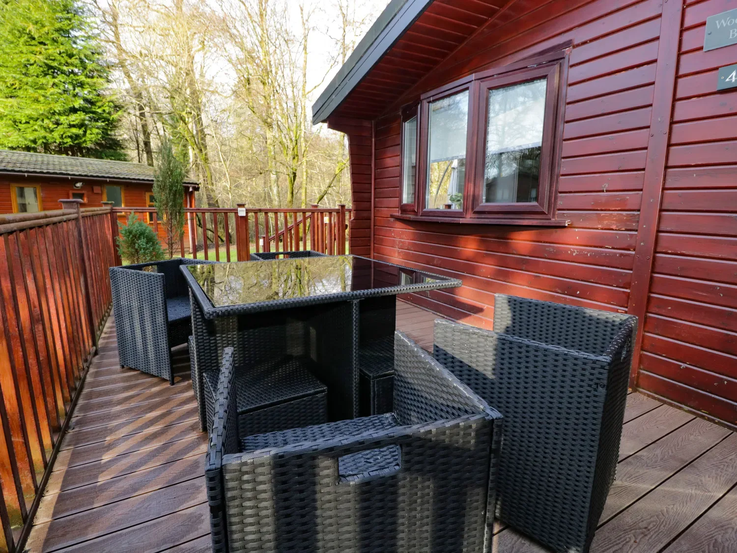 A wooden deck beside a red cabin has a black outdoor dining set.