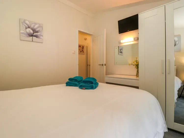 A bedroom with a neatly made bed and a mirrored vanity.